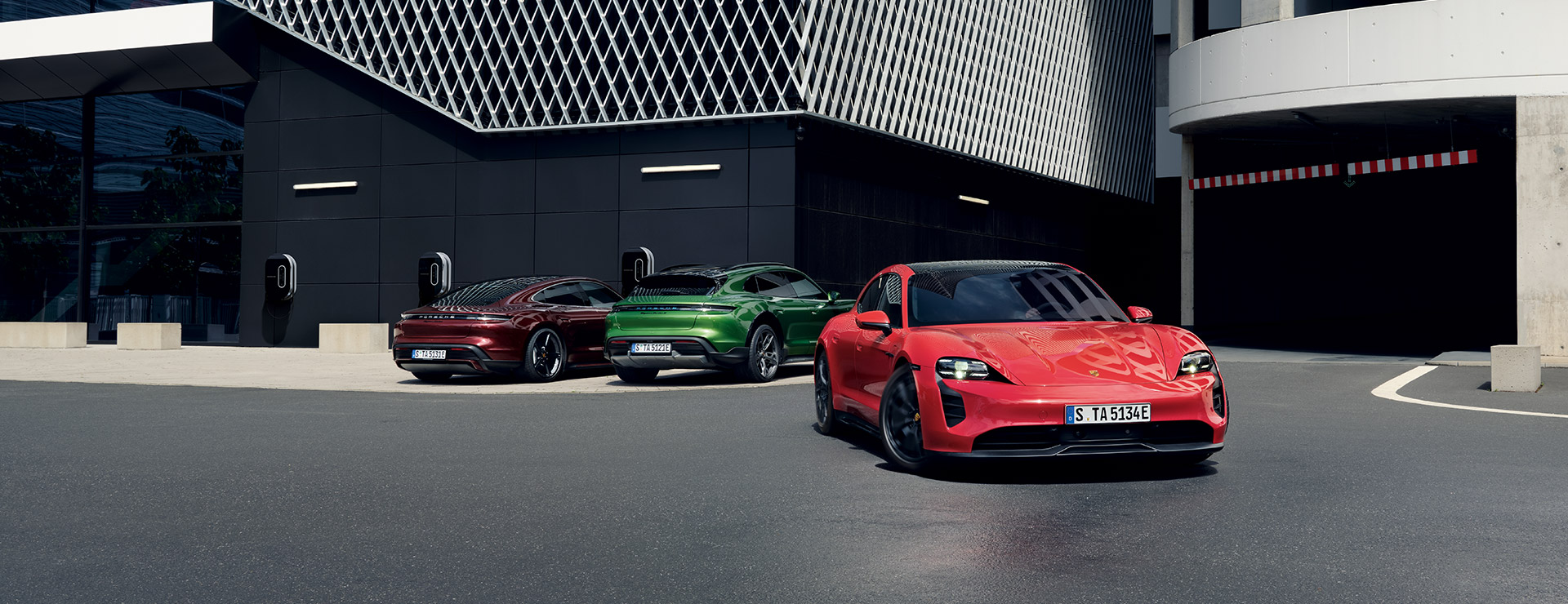 Verschiedene Porsche Taycan Modelle vor einem Parkhaus.